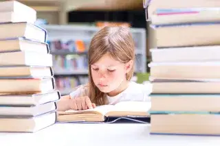 Kind zwischen Bücherstapeln liest ein Buch