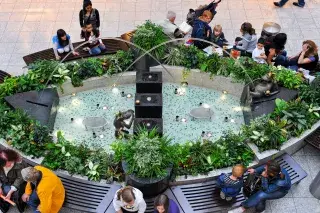 210206_oez-froschbrunnen_Olympia-Einkaufszentrum Menschen sitzen auf Bänken am Froschbrunnen im Olympia-Einkaufszentrum.