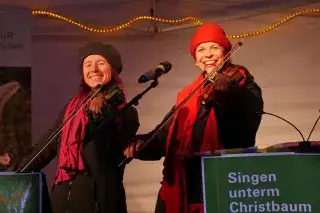 20210218_Singen_unterm_Christbaum_Christkindlmarkt Monika Drasch (links) und Traudi Siferlinger (rechts) singen mit Geigen unterm Christbaum auf dem Münchner Christkindlmarkt