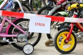 Zettel mit dem Wort "Streik" an einem Absperrband vor Kinderfahrrädern