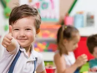 Ein Kind spielt in der Kinderbetreuung und zeigt den Daumen nach oben